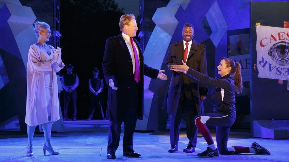 In this photo provided by The Public Theater, Tina Benko, left, portrays Caesar's wife, Calpurnia, and Gregg Henry, center left, portrays Julius Caesar during a dress rehearsal of The Public Theater's Free Shakespeare in the Park production of Julius Caesar in New York. Delta Air Lines is pulling its sponsorship of New York's Public Theater for portraying Julius Caesar as a Donald Trump look-alike in a business suit who gets knifed to death on stage. Late Sunday, Bank of America said it would withdraw its funding of the production. (Joan Marcus/The Public Theater via AP)
