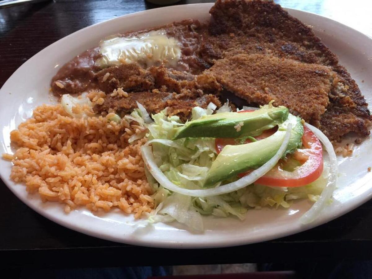 Milanesa – breaded steak or chicken breast – is served with rice, lettuce, tomatoes, and avocados.