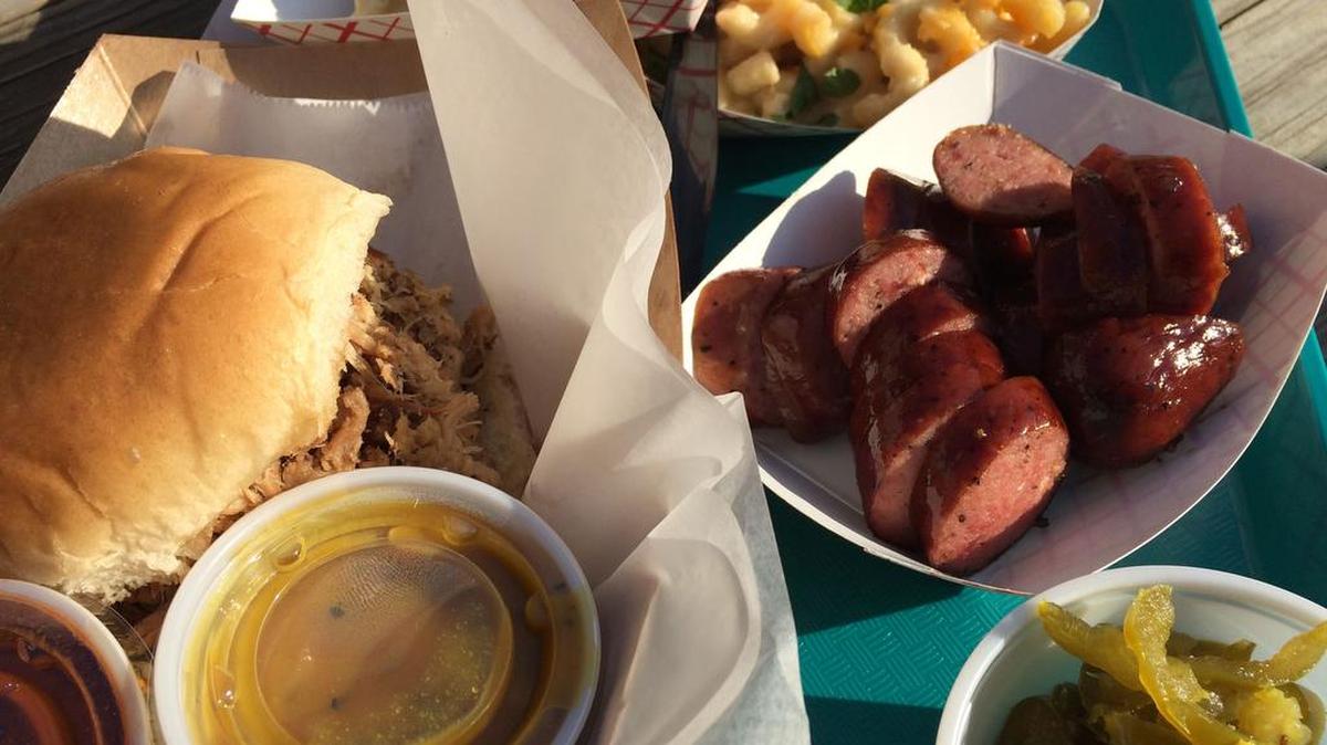 A sample selection from City Limits Barbeque in a 2017 photo: from far left, pulled pork sandwich with Texas red and Carolina yellow sauces; smoked gouda mac n’ cheese; mac n cheese with jalapeno; beef link; sweet pickled jalapenos.