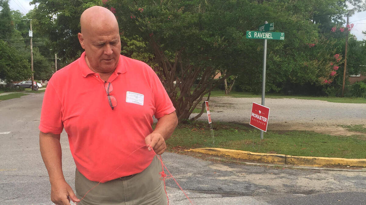 Poll worker Richard Schultz measures the distance between the entrance to Rosewood Elementary and campaign signs during the June 26, 2018 runoff election.
