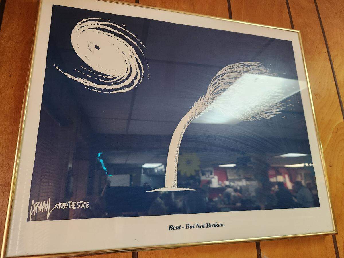 A framed political cartoon marking 1989’s Hurricane Hugo hangs at Mac’s Cash Grocery on Laurel Street in Columbia, SC.