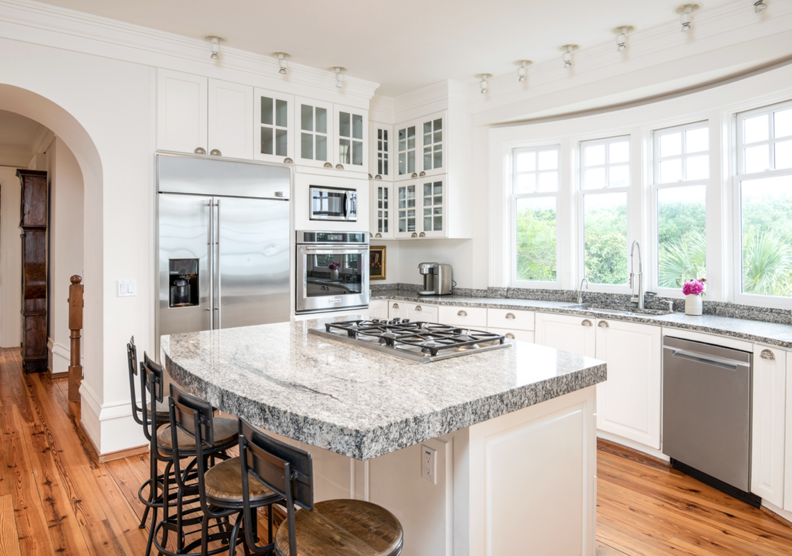 The kitchen has a rounded-arch pass-through to the dining room, center island with breakfast bar seating five and Dacor® gas cooktop, four windows over the sink, Georgia granite countertops, and glass-fronted upper cabinetry.