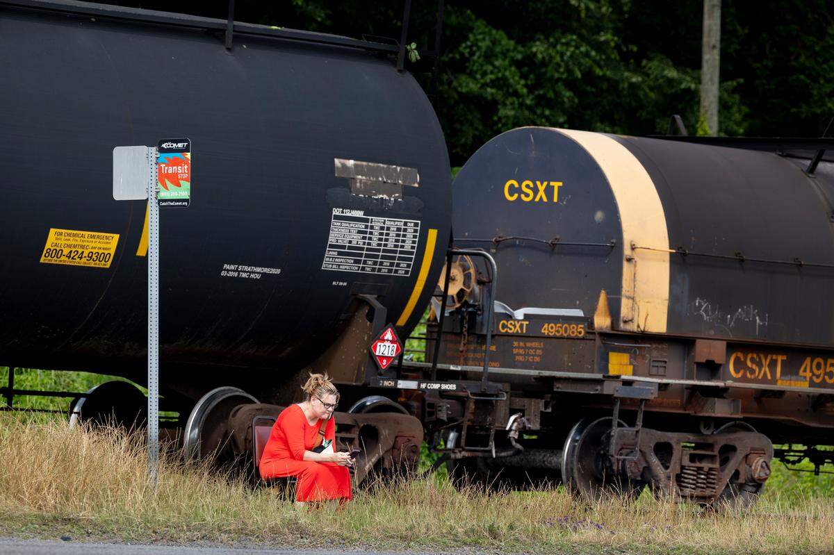 Patricia Tate waits for a bus along Assembly Street. A train carrying hazardous materials is idling on the train tracks behind her.