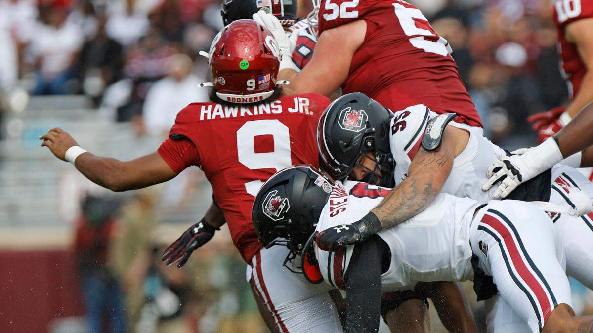 South Carolina’s Dylan Stewart (6), bottom, and Alex Huntley (95) bring down Oklahoma quarterback Michael Hawkins Jr. (9) after he was hit as he threw the ball in the first quarter, Saturday, Oct. 19, 2024, at Gaylord Family - Oklahoma Memorial Stadium in Norman, Okla. South Carolina intercepted the pass on the play.