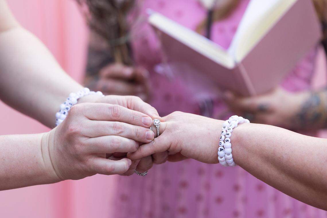 Christine Fowler places a ring on Sharon Thrailkill’s finger during their wedding at Y’all-Mart, a quarterly art fair series, at Art Bar in Columbia, South Carolina on Sunday, February 9, 2025. Fowler and Thrailkill met playing roller derby, and wore bracelets commemorating their time on a team together.