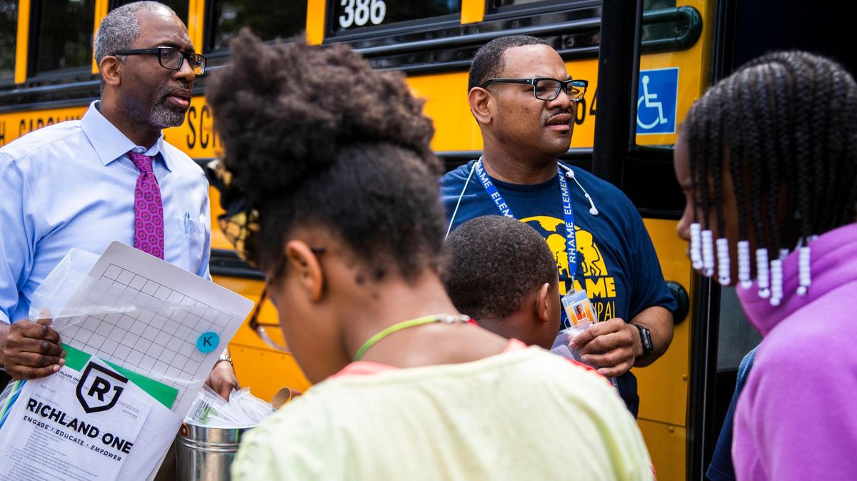 Richland 1 superintendent Dr. Craig Witherspoon and H.B. Rhame Elementary assistant principal Gregory Nelson scan the crowd to find kindergarten students and distribute work packets on Thursday, March 19, 2020. H.B. Rhame staff are taking the school busses to distribute the materials in student’s neighborhoods.