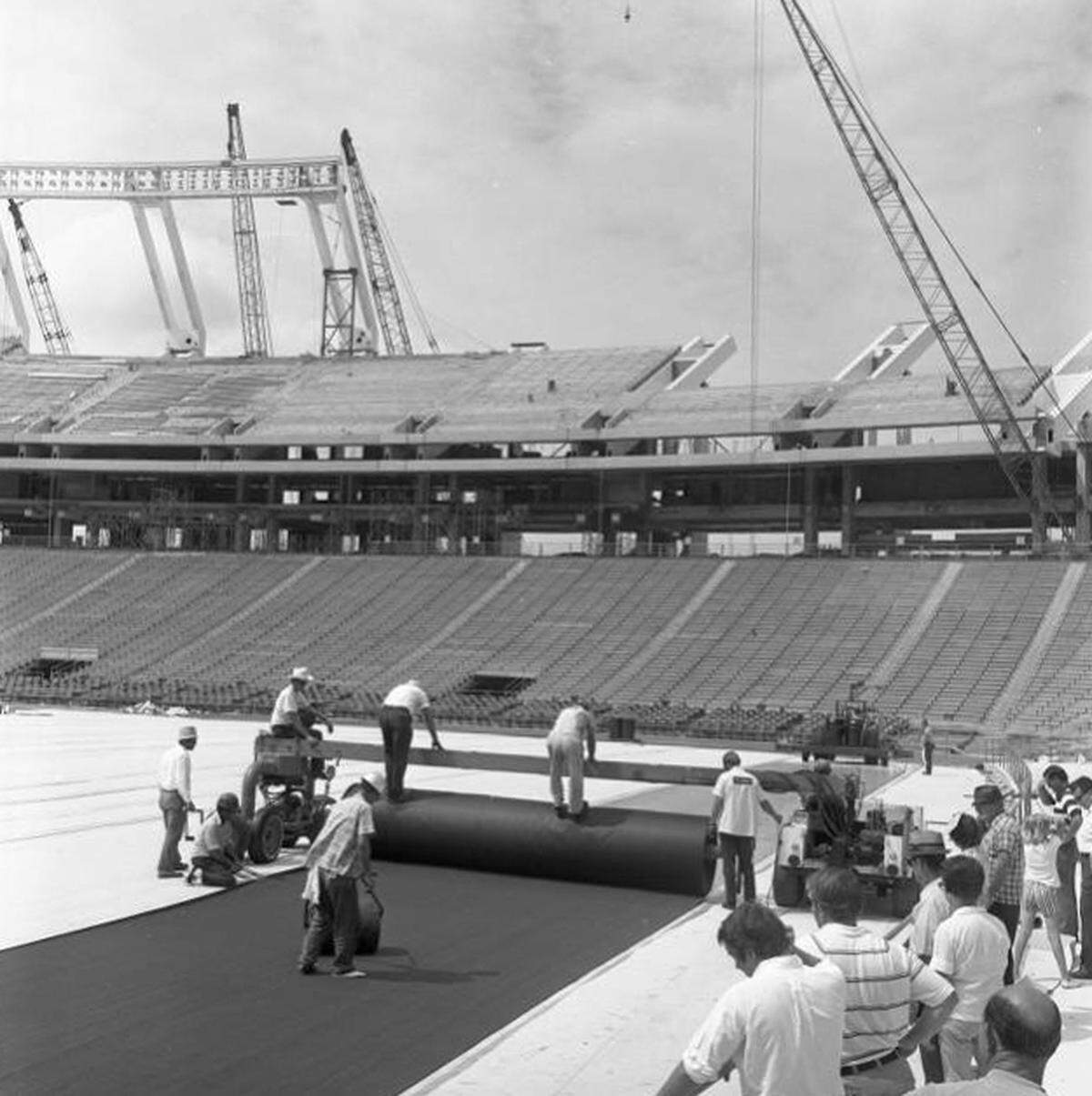Crews roll out the new AstroTurf surface at Carolina Stadium in 1971. Construction of the upper west deck is visible in the background.