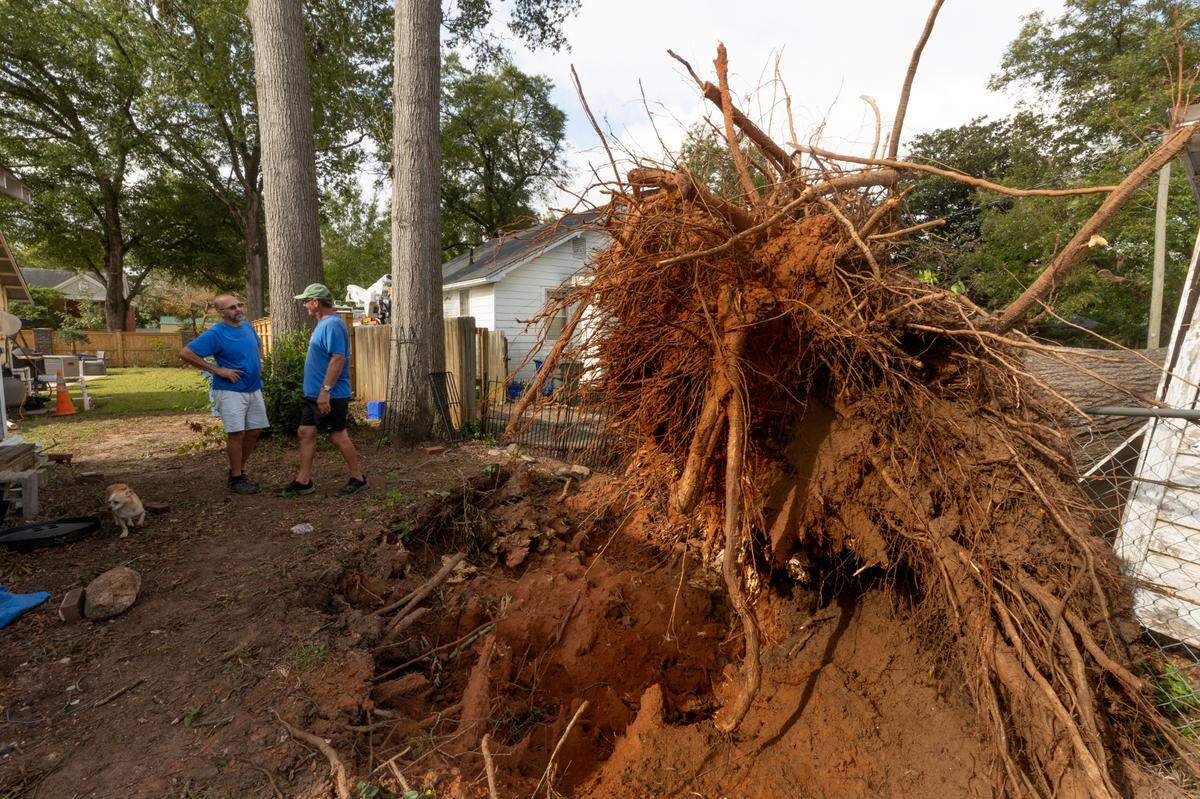 Stephen Wilcox, left, and Karl Kinard stand near where a large tree in Wilcox’s yard blew down, knocking power out to a portion of the neighborhood. Crews were able to repair the line almost a week after Hurricane Helene blew through.