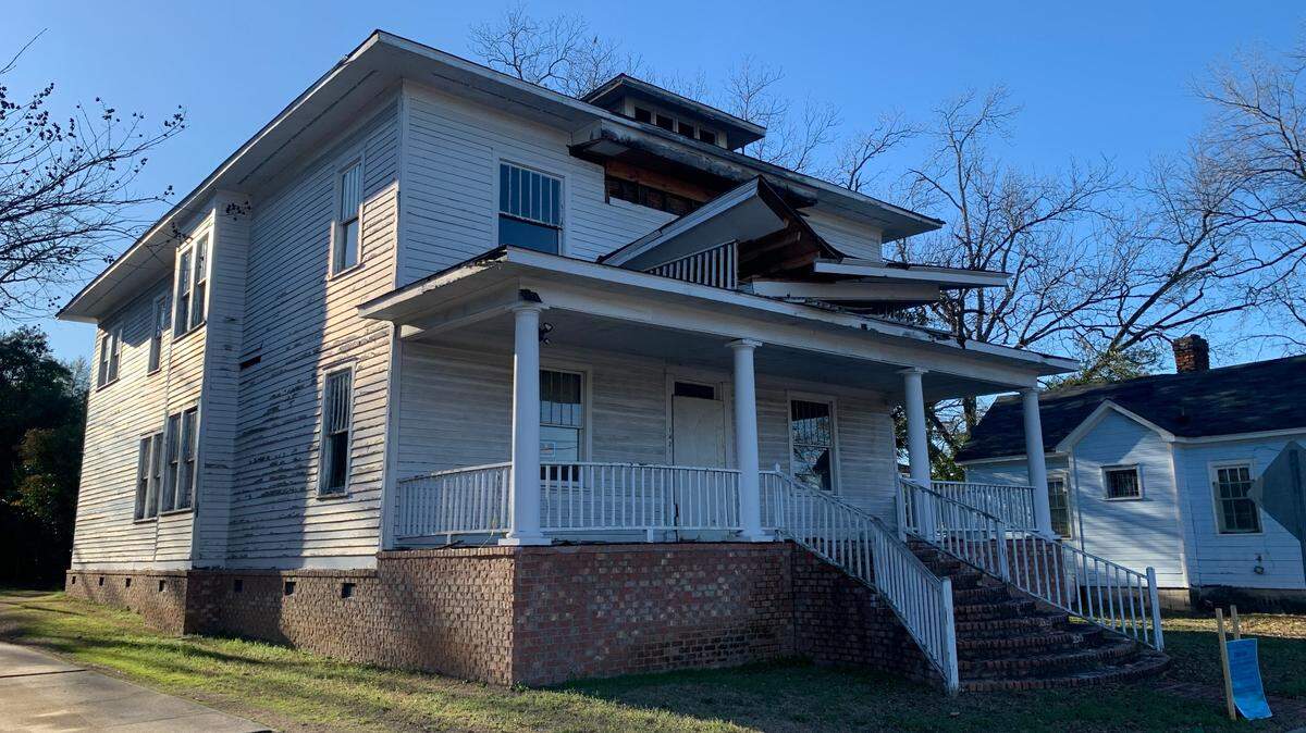 A photo of a two story historic house with the roof halfway demolished.