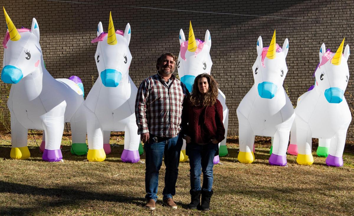 Ed and Tracy McDonnell pose for a portrait with their inflatable unicorns at their home in Columbia, South Carolina on Thursday, January 14, 2021. The family placed the unicorns at friends homes across their neighborhood, and slowly brought them back to their own yard.
