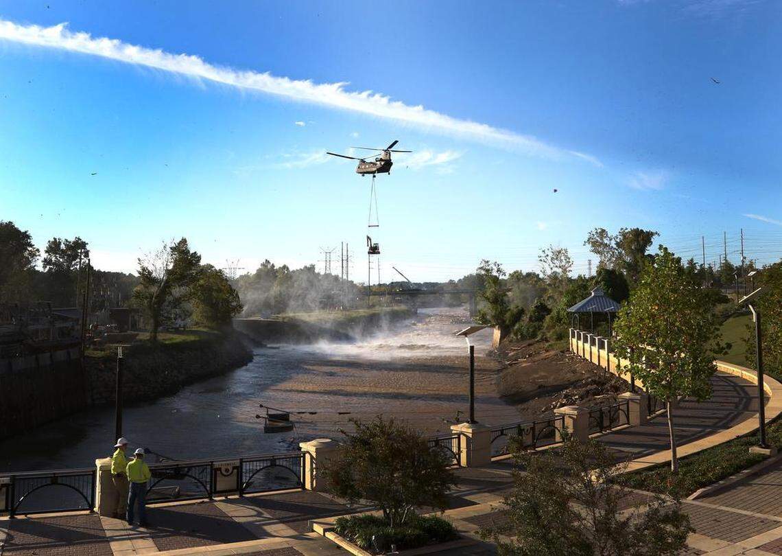 A military helicopter moves heavy equipment to aid in the repair of the Columbia Canal after the embankment gave way, draining the canal into the Congaree River.