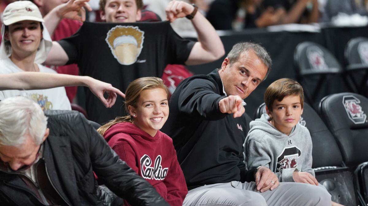 South Carolina head football coach Shame Beamer, pointing, sits with his daughter, Olivia Beamer, left, and son, Hunter Beamer, right, as a fan shows off his t-shirt depicting quarterback Spencer Rattler before an NCAA college basketball game against Kentucky Tuesday, Feb. 8, 2022, in Columbia, S.C. Kentucky won 86-76. (AP Photo/Sean Rayford)