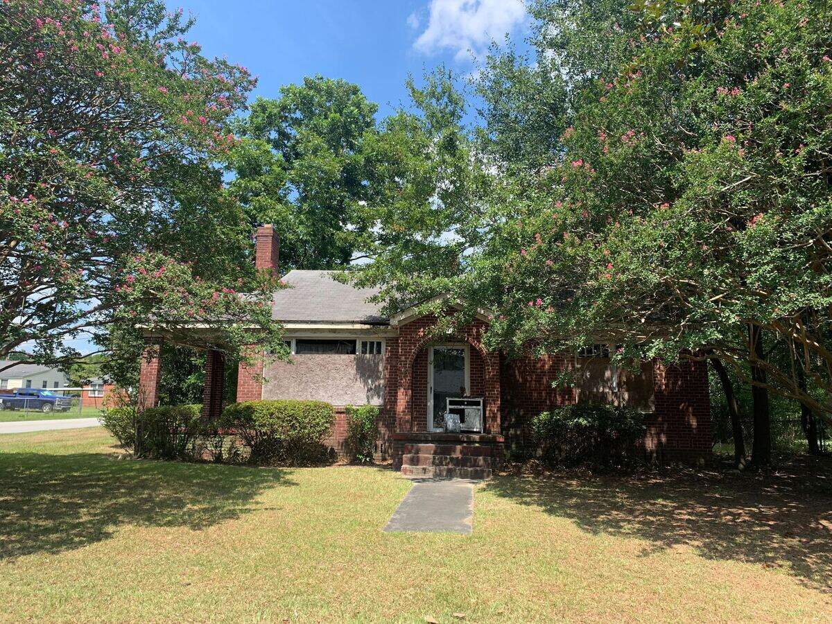 A red brick house with boards over the windows.