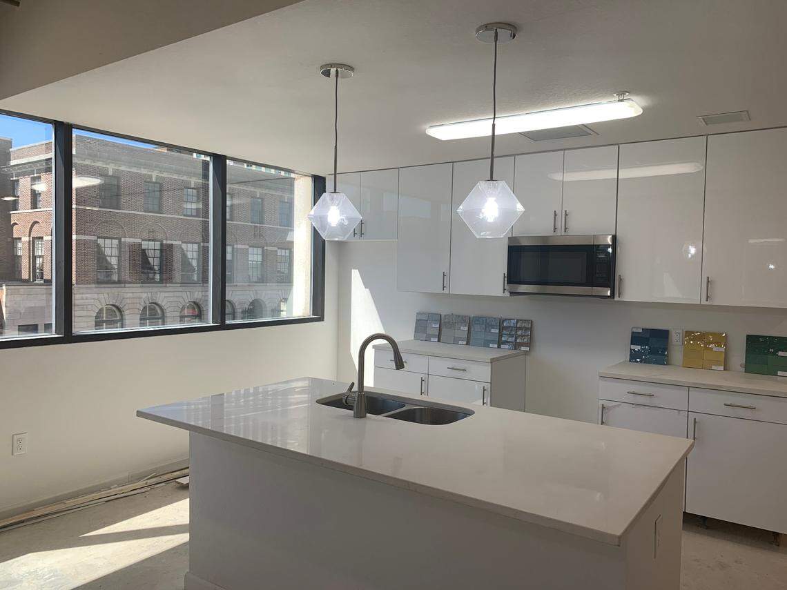 Developers are picking out backsplash and floor options for a kitchen in a one bedroom apartment at The Lady in Columbia. The apartment features art deco light fixtures and a modern white kitchen with windows across the entire kitchen space.