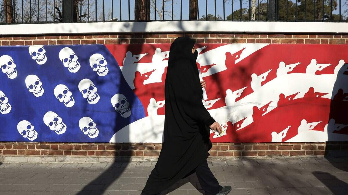 A mourner walk back from a funeral ceremony for Iranian Gen. Qassem Soleimani and his comrades, who were killed in Iraq in a U.S. drone attack on Friday, passing graffiti on the wall of the former U.S. Embassy in Tehran, Iran, Monday, Jan. 6, 2020. A push led by pro-Iran factions to oust U.S. troops from Iraq is gaining momentum, bolstered by a Parliament vote in favor of a bill calling on the the government to remove them. But the path forward is unclear. (AP Photo/Vahid Salemi)