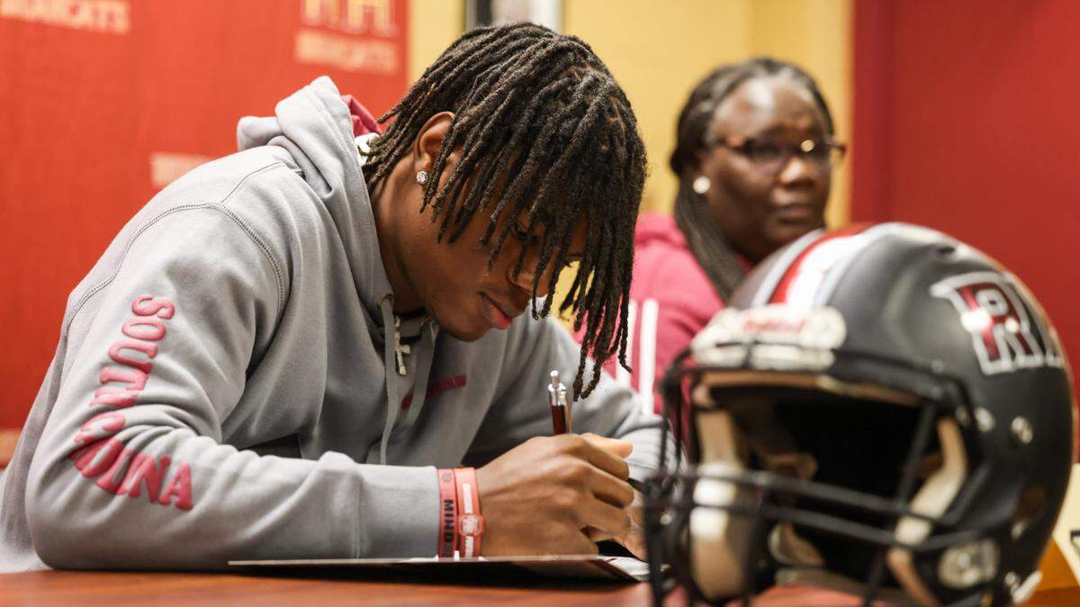 Malik Clark, a wide receiver from Rock Hill High School, signs paperwork during a signing day ceremony at his school on Wednesday, December 4, 2024.