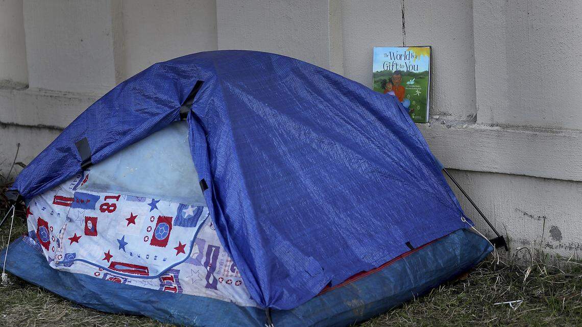 In this photo of a homeless encampment, a child’s book entitled: “The World is a Gift to You,” sits on the ledge of a sound barrier wall near a tent.