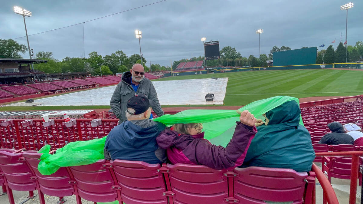 Nelson and Judy Travis and Becky Reynolds seek shelter under plastic while Ray Reynolds braves the rain during a weather delay at Founders Park on Friday, April 07, 2023. The University of South Carolina was about to play the third game in a series with LSU when the weather turned cold and rainy.