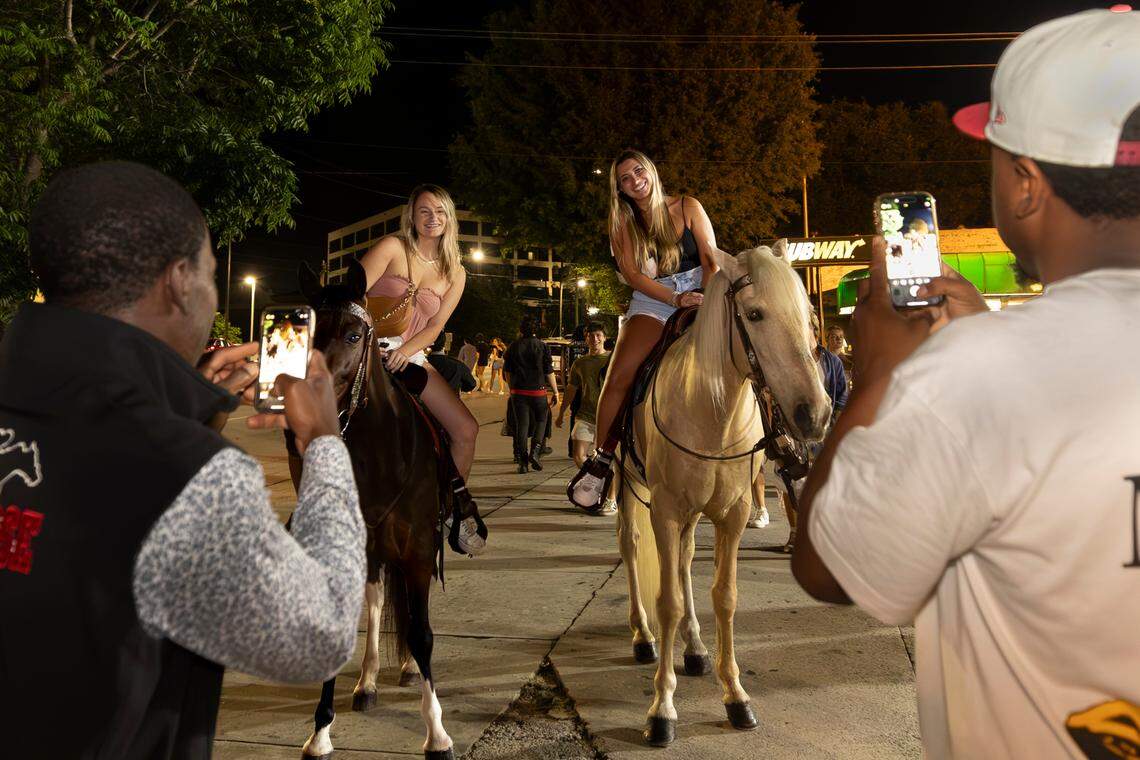 Stephen Harmon, left, and Brandon Mack photograph Faith McElwaine and Krista Kobi on Harmon’s horses in Columbia’s Five Points on Wednesday, May 10, 2024. Harmon charges students for rides and photo-ops.