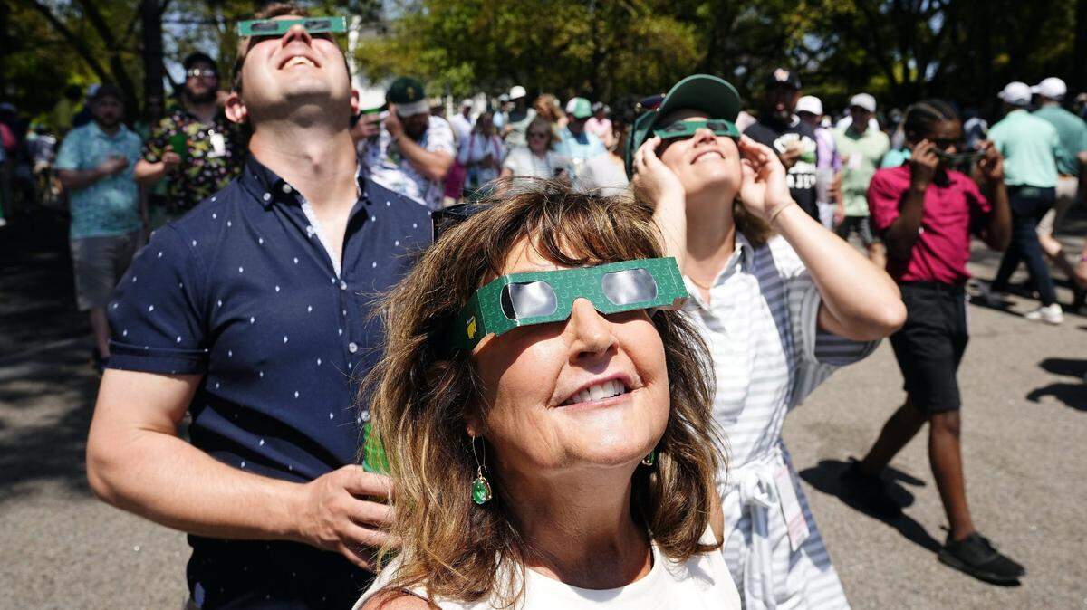 Betsy Kimbrough, Jim Kimbrough and Ali Rawlings watch the start of the eclipse Monday during a practice round for the Masters Tournament golf tournament at Augusta National Golf Club.