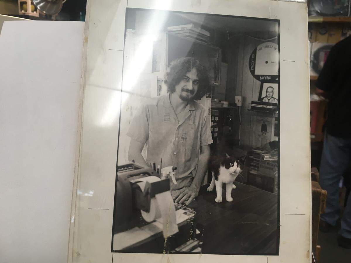 A picture of Tim Smith around 1985 at Papa Jazz with store cat Fred Two sits behind the counter of the record store.