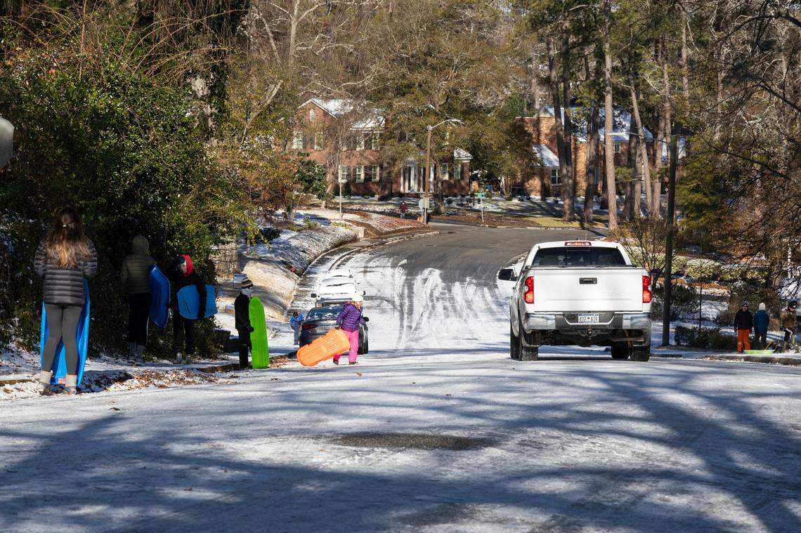 Children sled as trucks attempt to control their cars as they slide down an icy hill in Columbia, South Carolina on Wednesday, January 22, 2025.