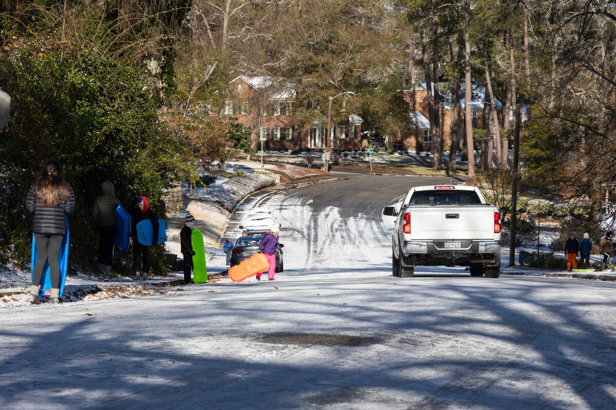 Children sled as trucks attempt to control their cars as they slide down an icy hill in Columbia, South Carolina on Wednesday, January 22, 2025.