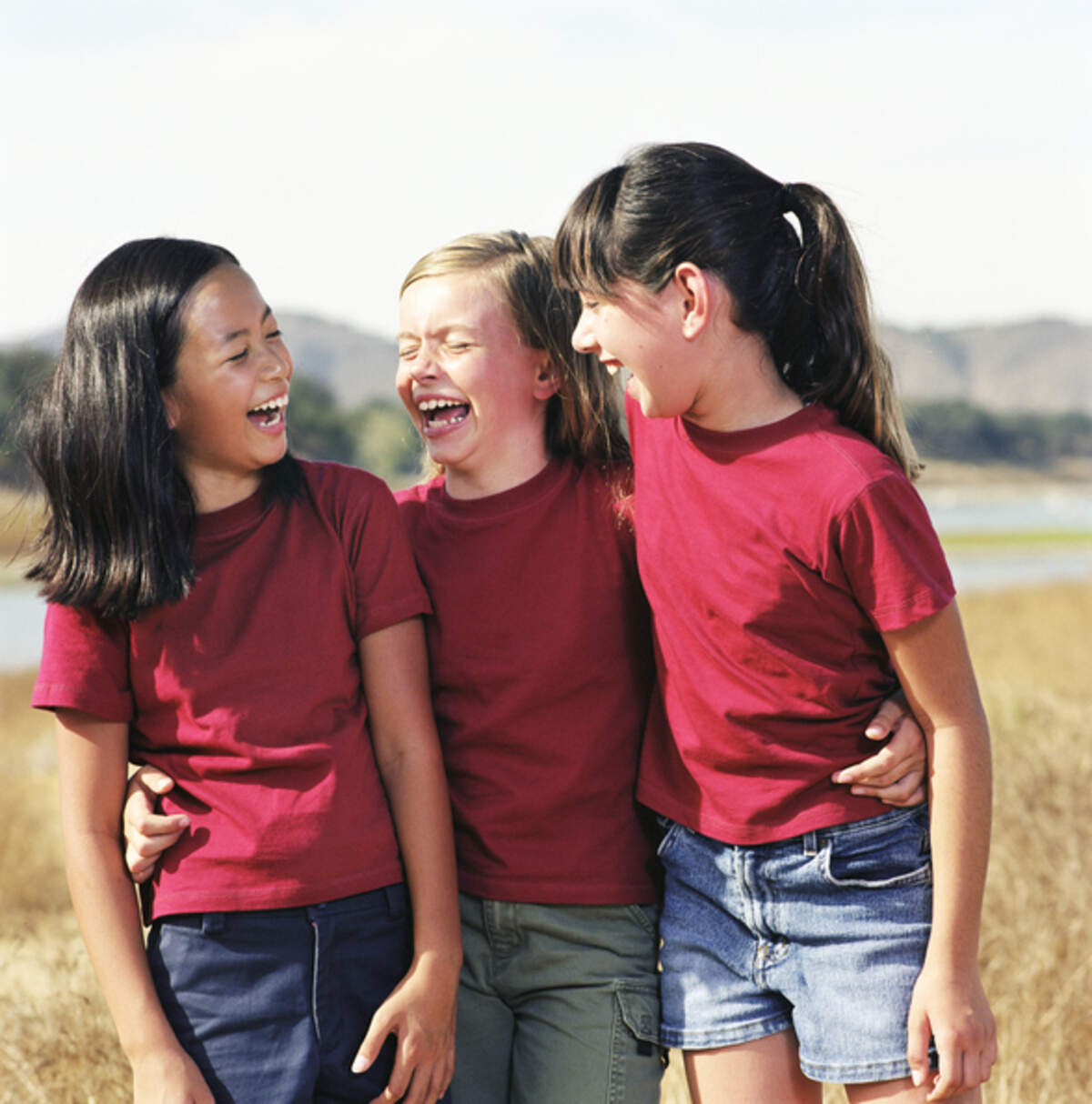 Three girls (8-10) standing with arms around each other, laughing