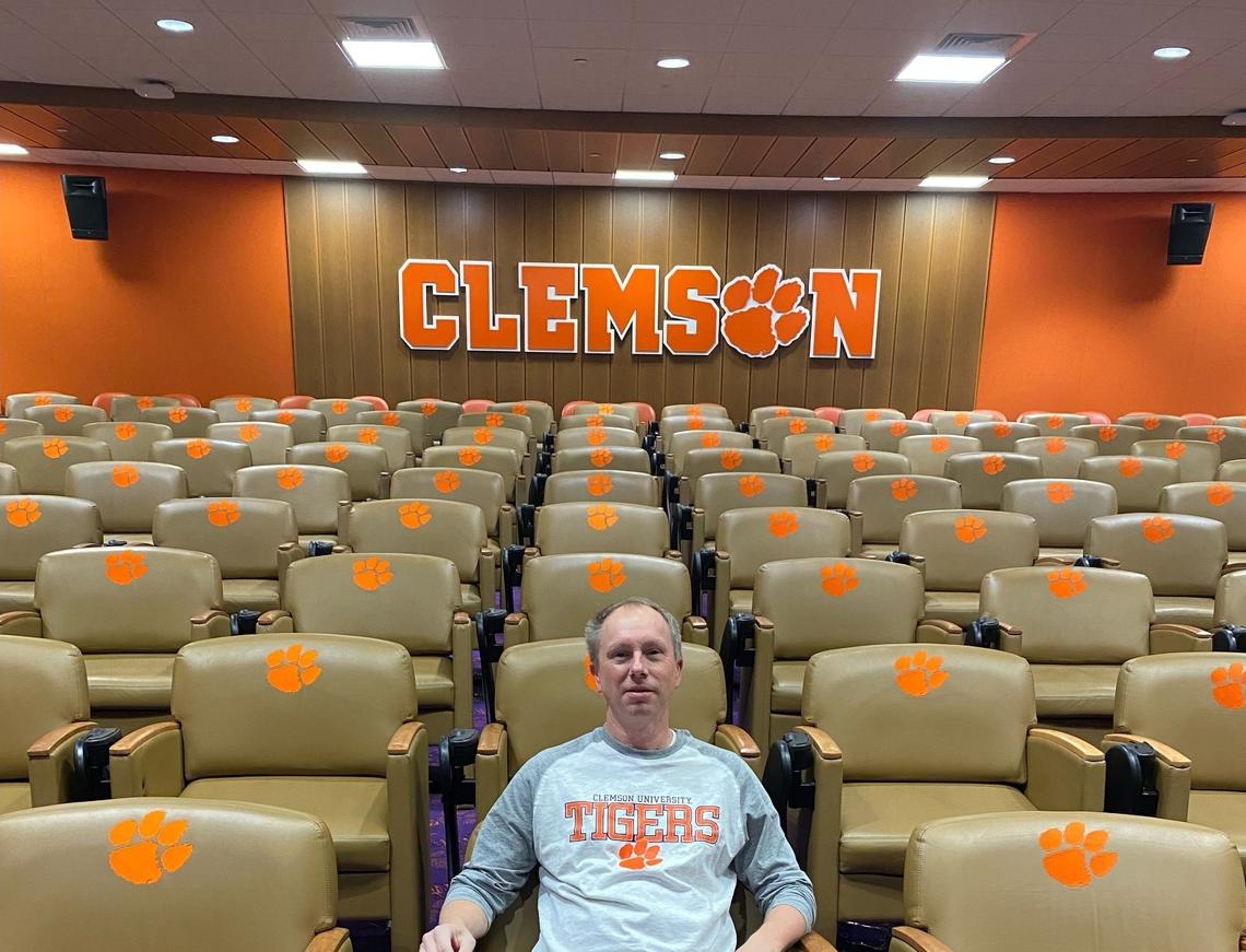 Clemson fan Brian Darby poses for a photo in a team meeting room at the Allen N. Reeves Football Complex on Nov. 30, 2023, during a tour with Tigers offensive lineman Tristan Leigh.