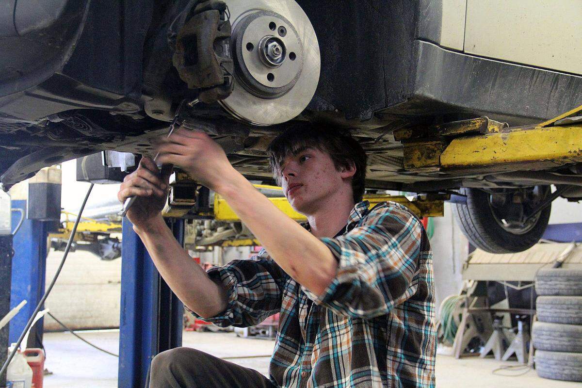 A high school student repairs a car in an automotive shop class. Jobs in automotive body repair are relatively safe from automation, and they don’t require a college degree.