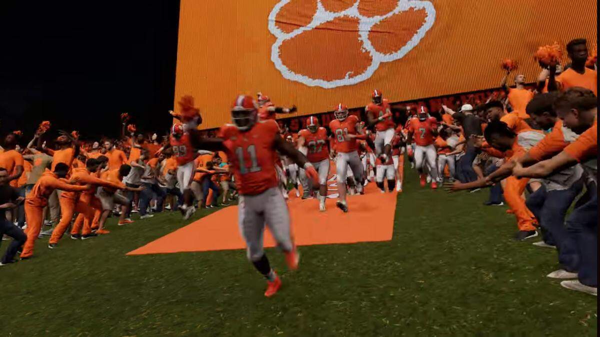 Surrounded by student fans, virtual Clemson football players run down The Hill in the east end zone of Memorial Stadium for a night game in EA Sports College Football 25. Behind them is Clemson’s video board, which was updated in 2022 and is one of the largest in the country.