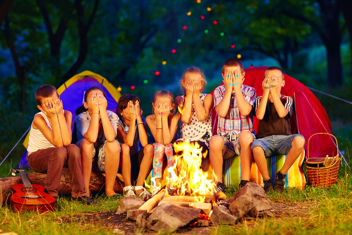 kids with painted faces on hands sitting around camp fire