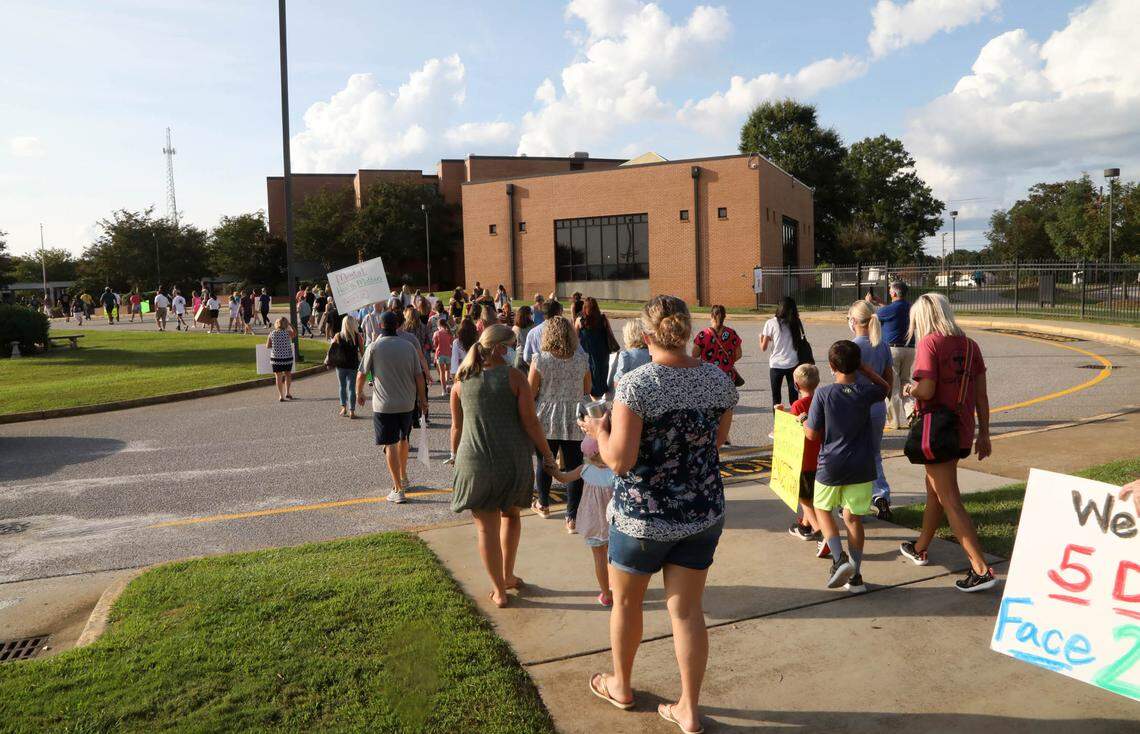 Parents and students cary signs and chant in front of Irmo High School before a district board meeting. The group is pushing the district to allow 5-day-a-week in person education.