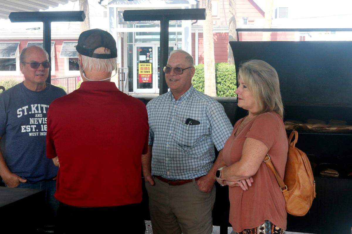 Maurice’s Piggie Park BBQ owners Lloyd and Paul Bessinger (center) talk with a couple that came to ask about the business on Nov. 1, 2024. The West Columbia restaurant has temporarily moved smokers under the awnings in its parking lot to start cooking again after its cooking facility was lost to a fire last month.
