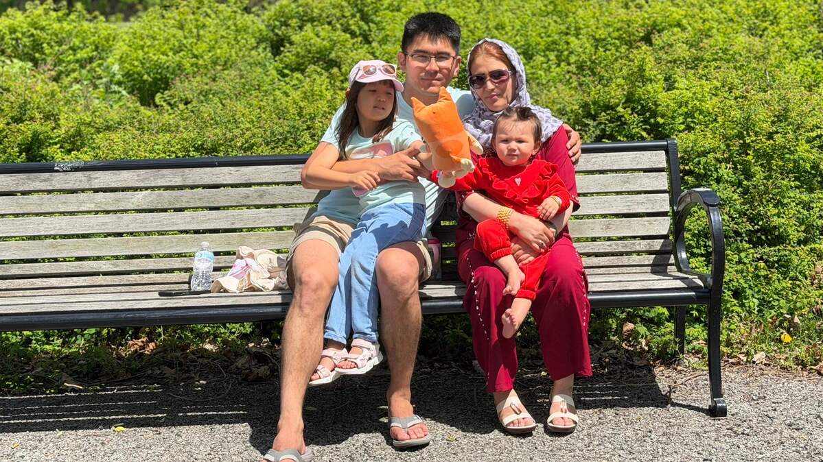A family sit on a sun-drenched park bench.