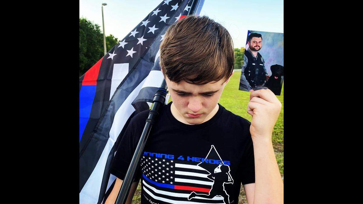 Zechariah Cartledge, founder of the nonprofit Running 4 Heroes, holds a flag and a photo of Cayce Police Officer Roy Andrew “Drew” Barr, before running a mile in his honor. Barr was shot and killed on Sunday.