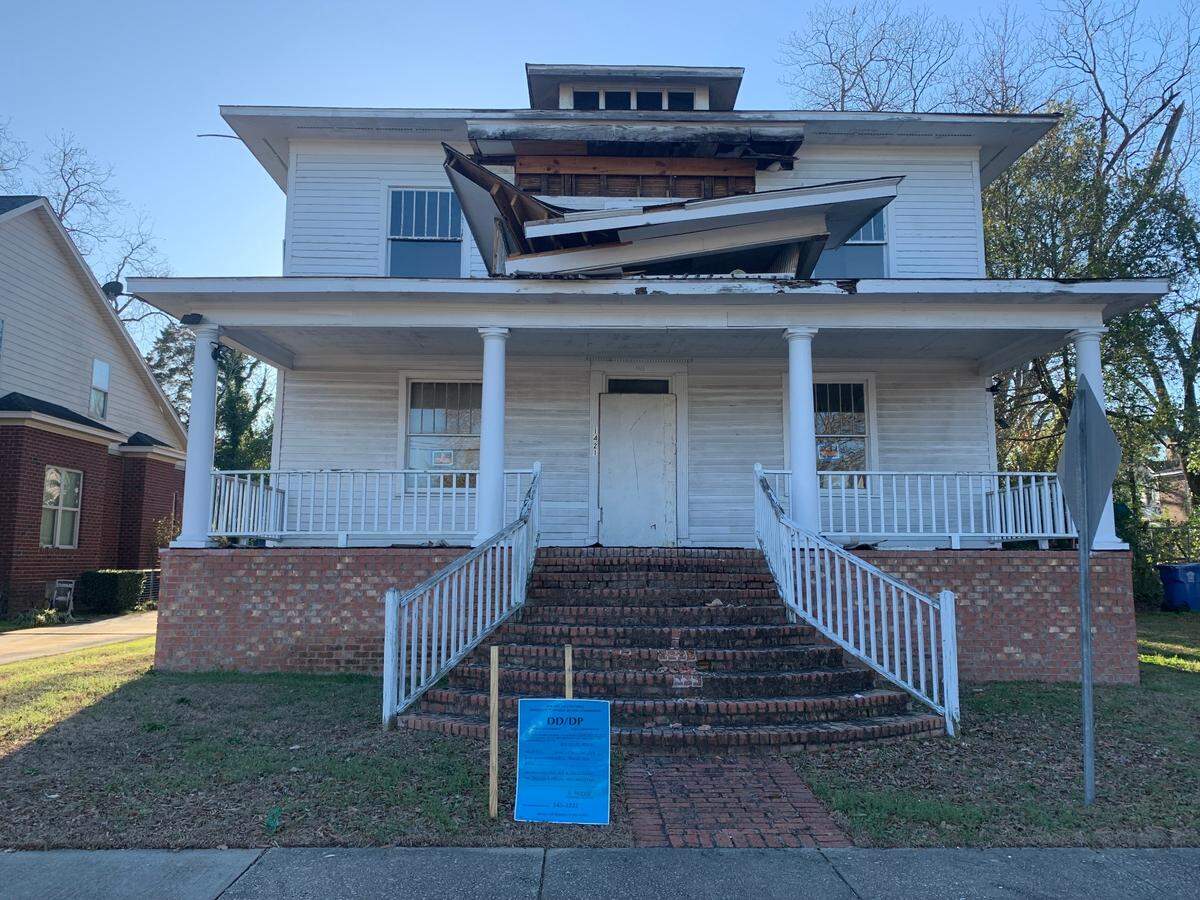 A photo of a two story historic house with the roof halfway demolished.