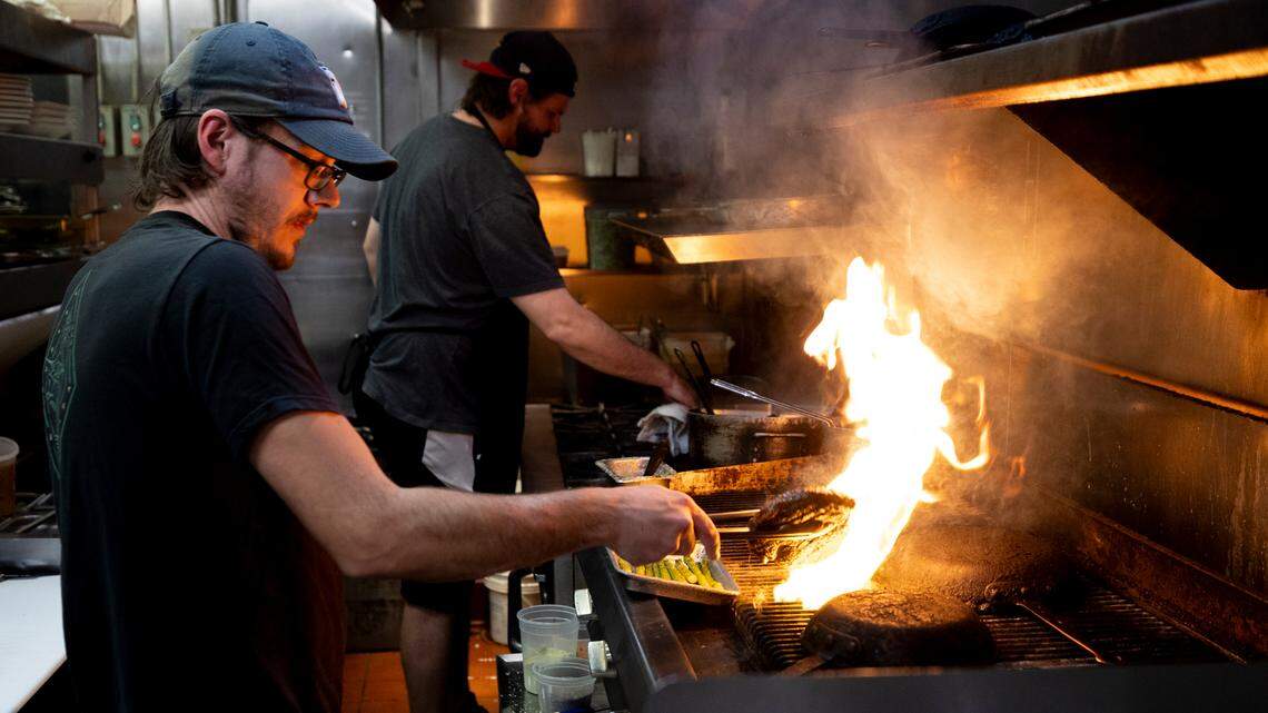 Daniel Whalen, left, prepares steaks on the grill as Dieter Steinborn starts a dish at Saluda’s Restaurant.