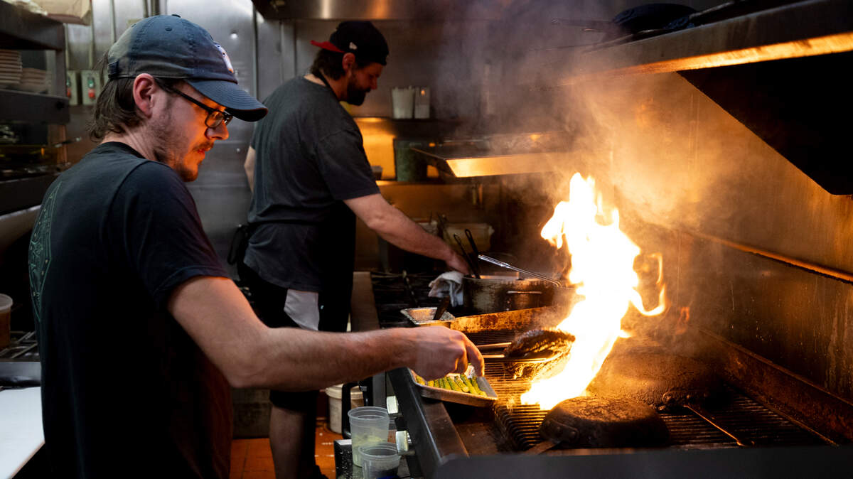 Daniel Whalen, left, prepares steaks on the grill as Dieter Steinborn starts a dish at Saluda’s Restaurant.