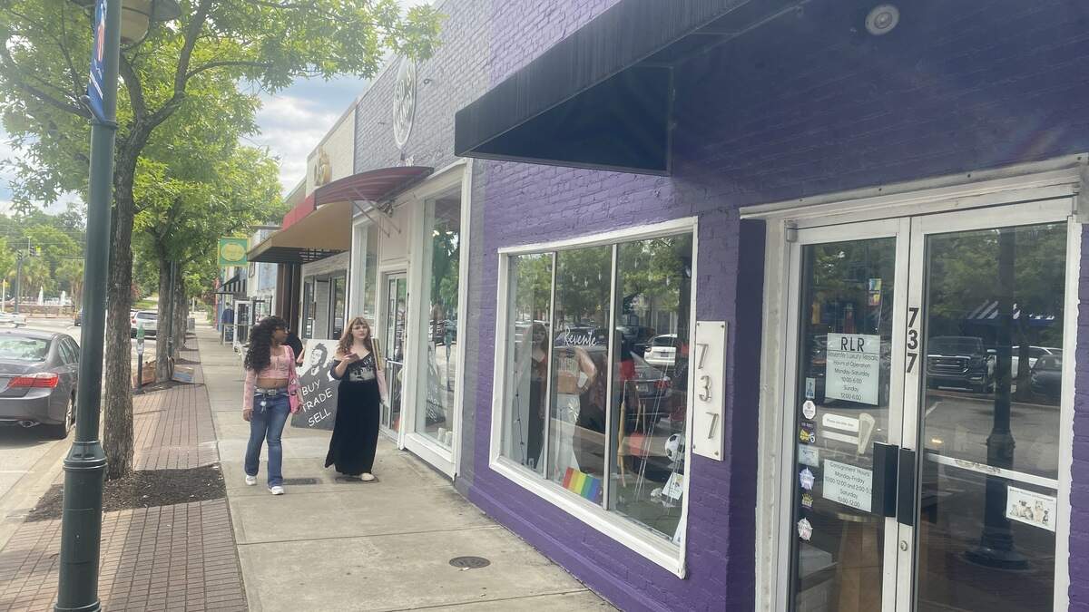 Two young women walk by a line of storefronts, one of them purple.