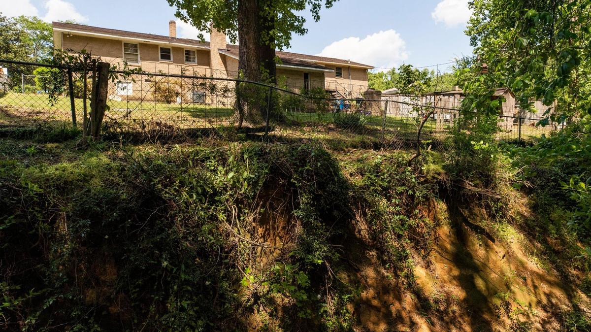 Karen Dawkins home in Cayce, South Carolina is visible next the fast-encroaching banks of a creek on Wednesday, April 21, 2021. Years ago her family had enough yard behind the fence they needed to mow in an area that no longer exists.