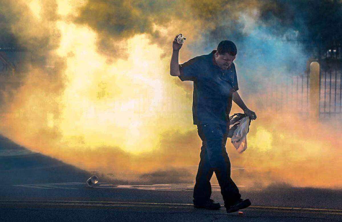 A man walks through a cloud of tear gas as police disperse crowds gathered during peaceful rally to protest the killing of George Floyd that escalated into a riot with groups breaking into businesses and burning police cars in the Columbia Vista.