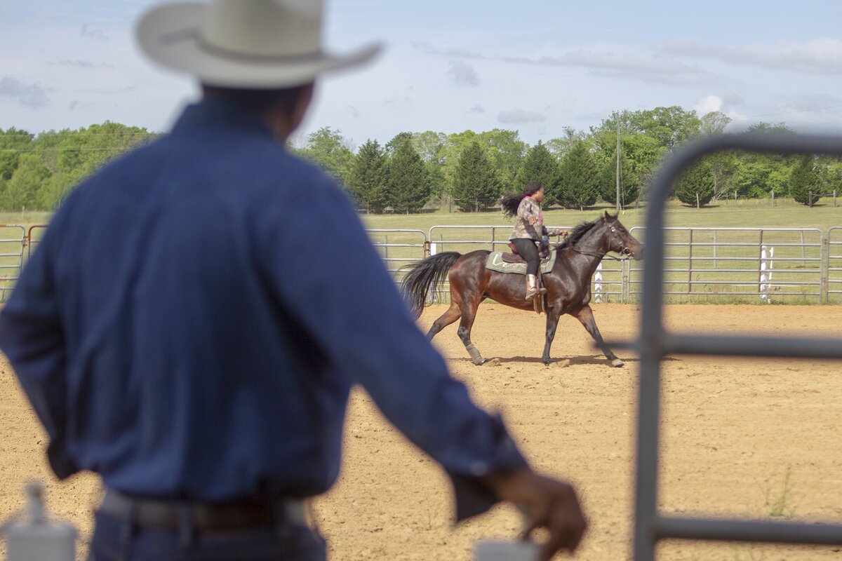 Mark Myers watches his granddaughter, Zyarriah Myers, 16, ride along the arena with her horse Coco, a 10-year-old Quarter Horse, on her grandparents ranch in Rembert, SC. Myers will be participating in rodeo events during the Black Cowboy “Man or Myth” African-American Cultural Festival. Mark Myers began the event more than two decades ago to share the history of the black cowboy.
