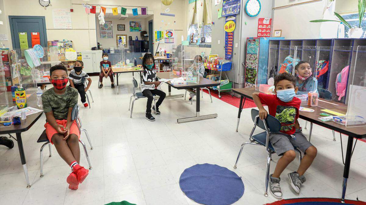 First-graders sit in a classroom on Wednesday, Aug. 18, 2021, the first day of school at A.C. Moore Elementary School. Social distancing, masks and plexiglass dividers help prevent the spread of The Coronavirus.
