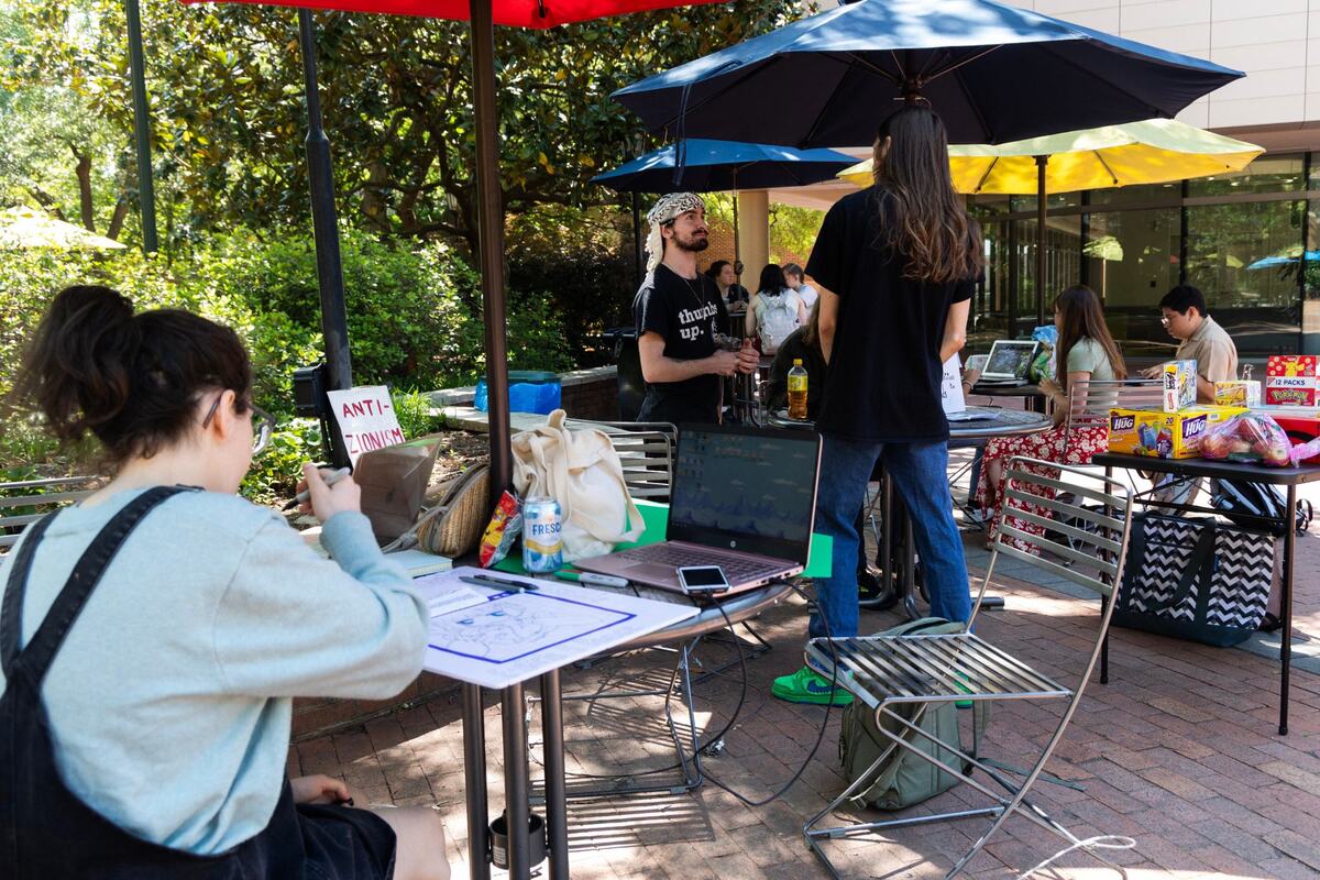 University of South Carolina students and other pass out snacks and hold sign in the sitting area behind the Russell House on the university’s campus on April 24, 2024.