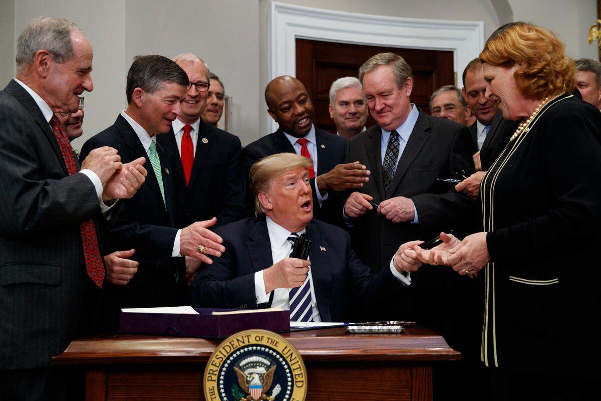 President Donald Trump hands out pens after signing the "Economic Growth, Regulatory Relief, and Consumer Protection Act," in the Roosevelt Room of the White House, Thursday, May 24, 2018, in Washington.