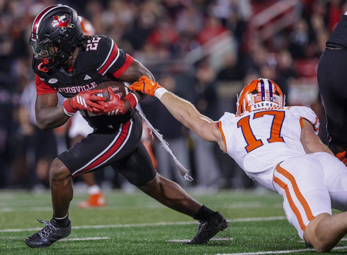 Keyjuan Brown #22 of the Louisville Cardinals runs the ball as Wade Woodaz #17 of the Clemson Tigers reaches for the tackle during the first half of the NCAA football game between the Louisville Cardinals and the Clemson Tigers at L&N Federal Credit Union Stadium on November 14, 2025 in Louisville, Kentucky.