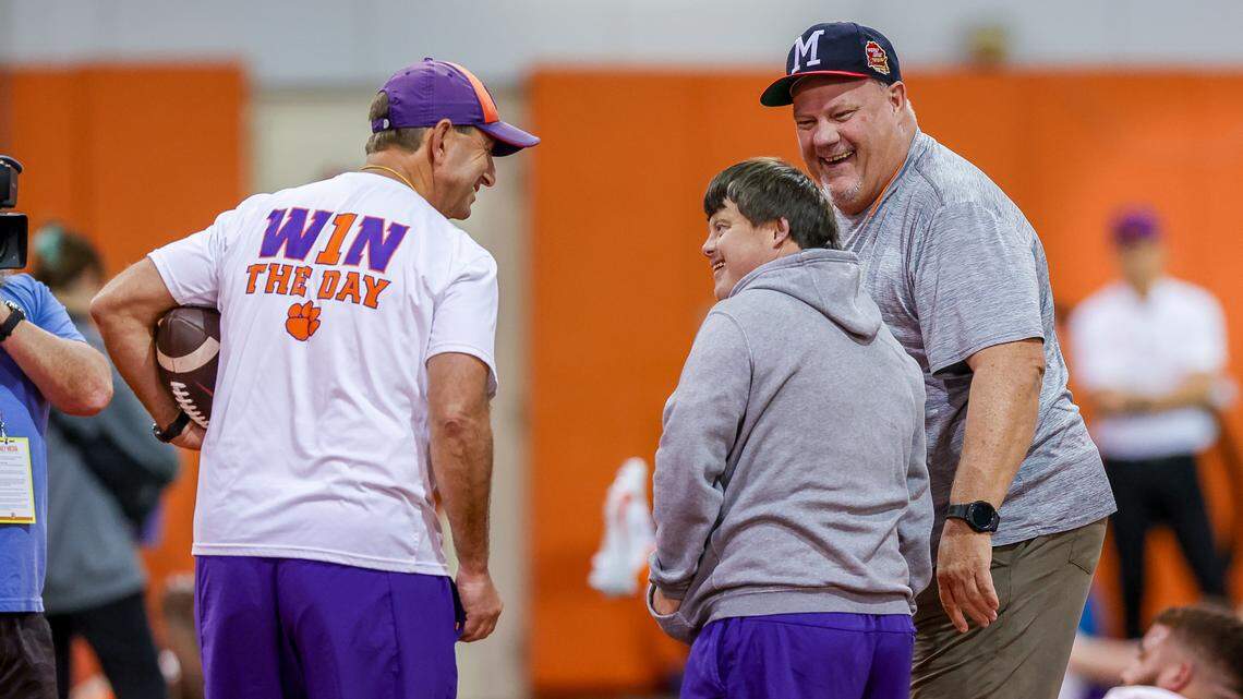 Clemson football coach Dabo Swinney (left) and TigerNet.com reporter David Hood (right) present team equipment manager David Saville (middle) with $650 in gift cards as a surprise birthday present on Friday, March 1, 2024, at the team’s indoor practice facility. Saville, who has Down syndrome, had requested Chick-fil-A gift cards for his 34th birthday.