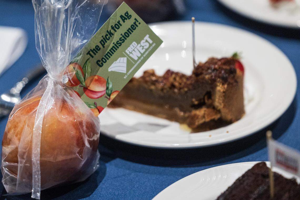 A peach wrapped in an advertisement for Fred West’s campaign for Commissioner of Agriculture next to a slice of cake with an advertisement for Alan Wilson’s primary bid for governor at the Silver Elephant Dinner, the South Carolina Republican Party’s biggest fundraiser of the year, at the Columbia Convention Center on Saturday, August 9, 2025.