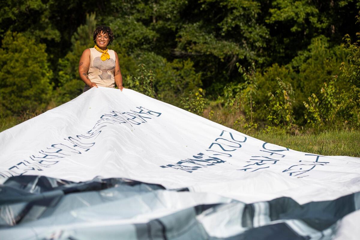 Sadia Pollard unrolls old billboards at their farm in Lugoff, South Carolina on Saturday, June 19, 2021. Pollard will place the billboards over their tilled field, and the heat under the tarp will kill any remaining weeds.